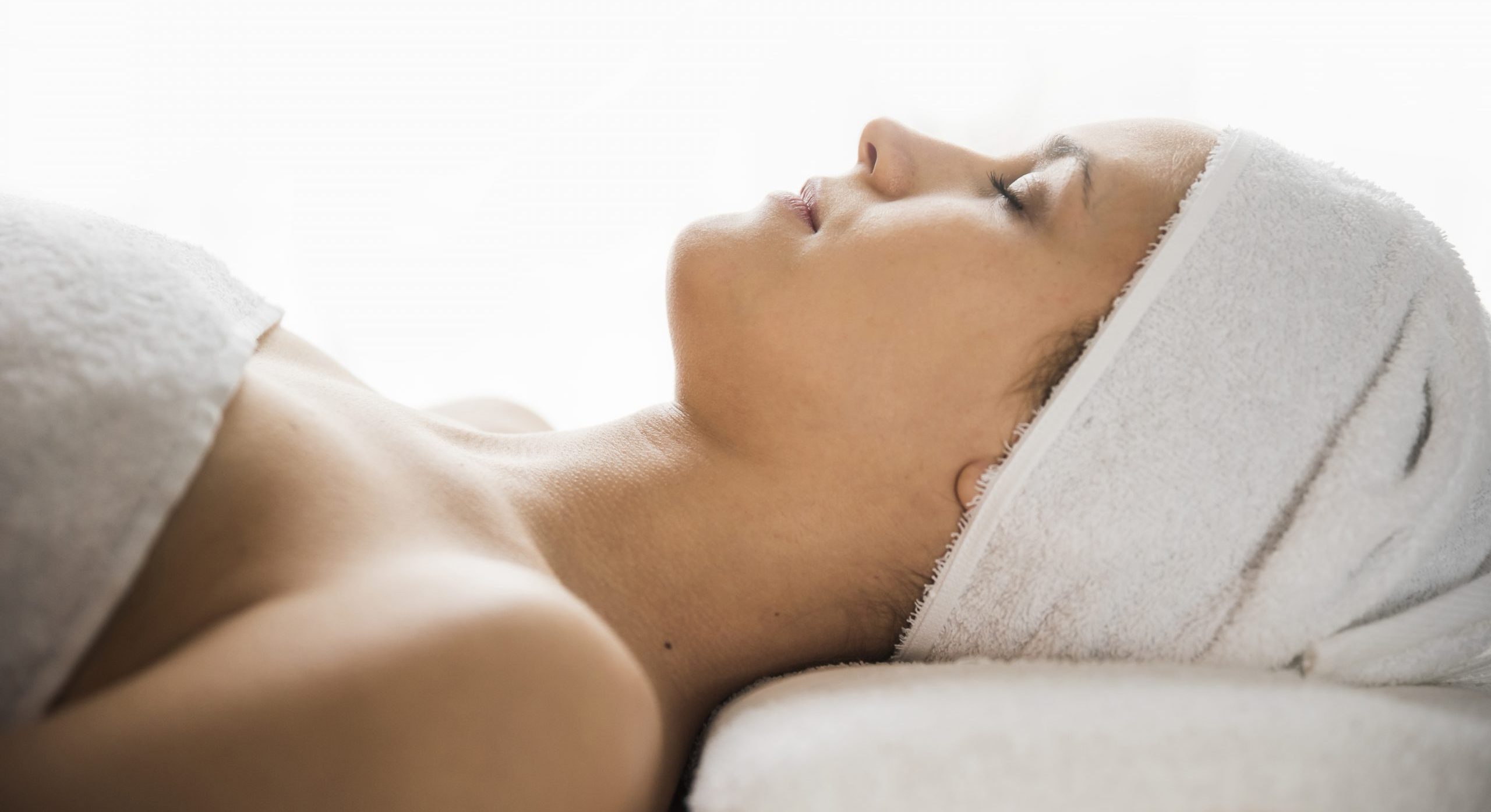 vue-cote-de-jeune-femme-a-serviette-enveloppee-sur-tete-dormir-sur-lit-massage-contre-toile-de-fond-blanc